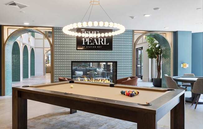 A pool table with a lighted sign that says "PEARL" behind it.