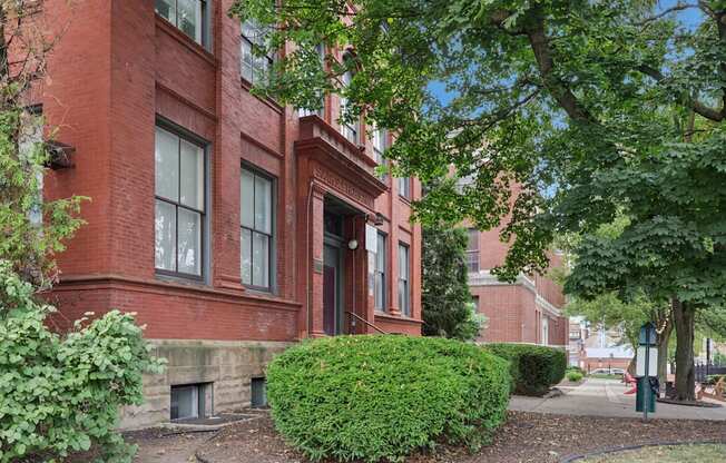 A red brick building with a green bush in front.