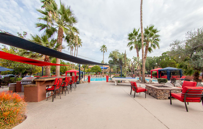 a patio with red chairs and tables and a pool with palm trees
