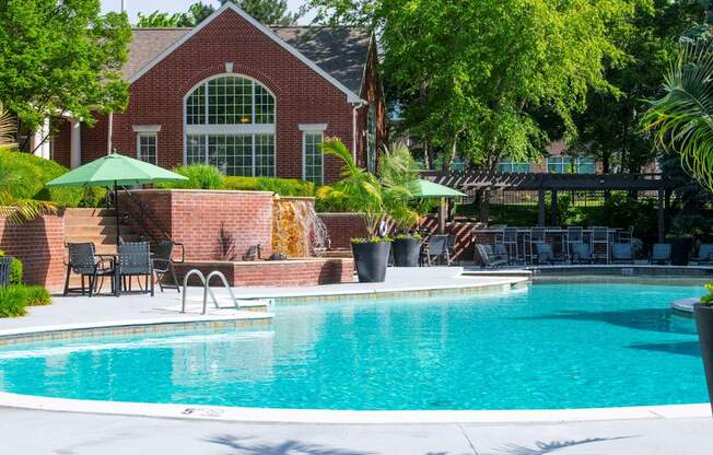 A pool in front of a house with a green umbrella.