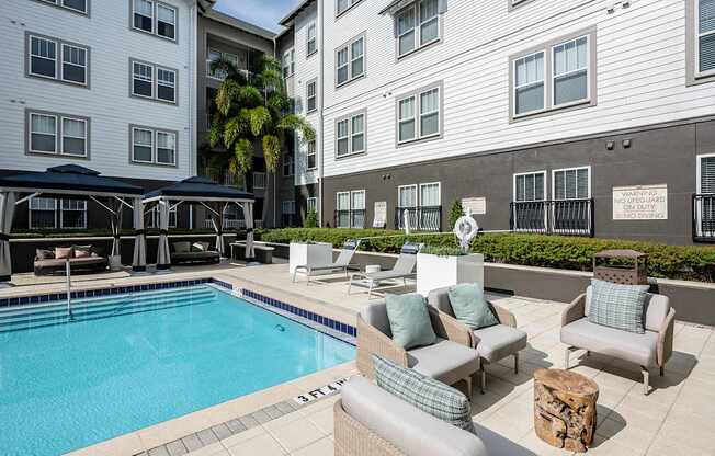 A pool surrounded by chairs and cushions with a building in the background.