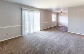 an empty living room with a large window and a ceiling fan