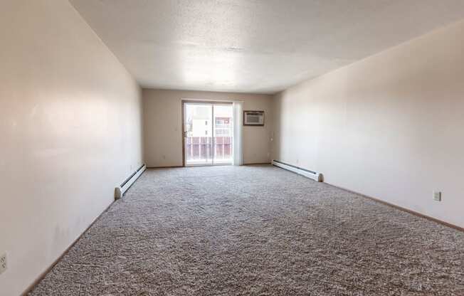 Grand Forks, ND Cherry Creek Apartments. A vacant living room in the unit 223 with a glass sliding door and white walls with a carpeted floor.