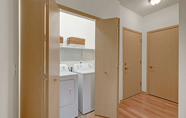 A convenient laundry closet here at Swan Creek with in-unit washer and dryer, warm wood doors, and bright lighting, creating a practical, clean, and easy-to-access utility space.