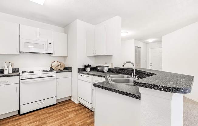 Virtually staged kitchen with white appliances, wood flooring, gas stove, white cabinetry, gray speckled countertop