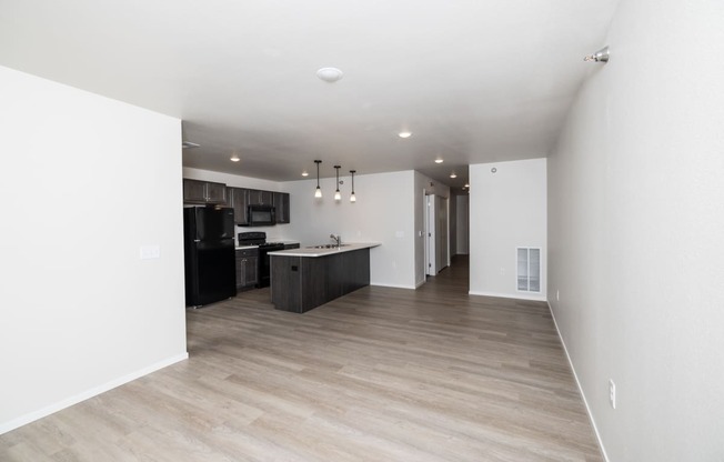 an empty living room and kitchen with white walls and wood flooring