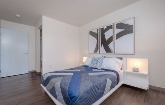 Bedroom in an apartment furnished with a queen-size bed, two nightstands, vinyl flooring, and high ceiling