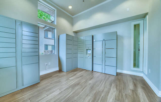 A room with wooden floors and white walls, featuring a row of white cabinets and a window.