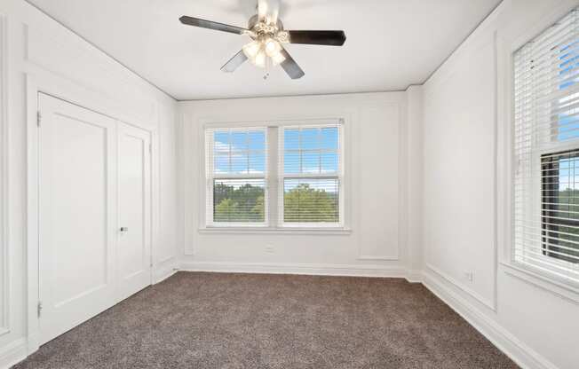 an empty bedroom with a ceiling fan and two windows