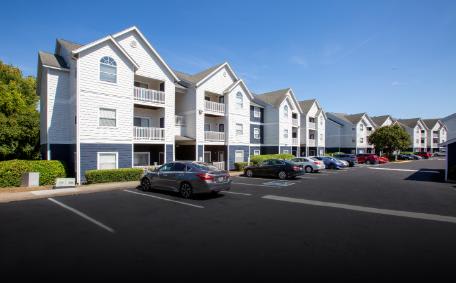 A row of white and blue apartment buildings with cars parked in front.