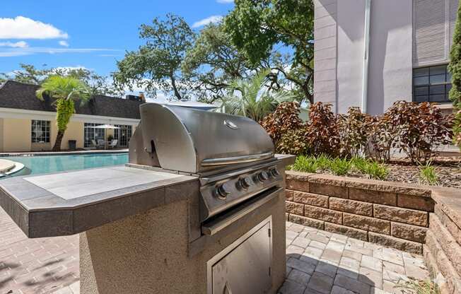 A modern outdoor kitchen with a built-in grill and a pool in the background.