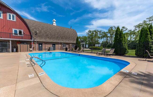 A large outdoor swimming pool with a red barn in the background.