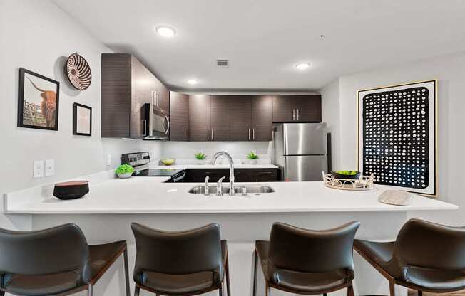 A modern kitchen with a white countertop and brown chairs.