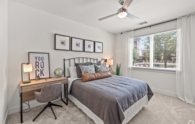 A bedroom with a bed, desk, chair, and pictures on the wall.