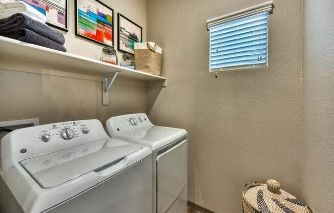 The Craft at Gilbert and Baseline apartment utility room showing top loading clothes washing machine and top loading dryer with small window and shelf