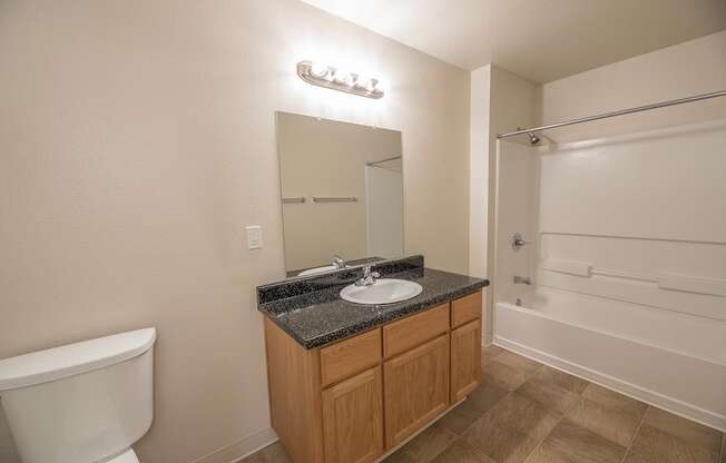 A bathroom with a toilet, sink, mirror, and bathtub at Autumn Oaks Apartments, Roseville, CA, 95678
