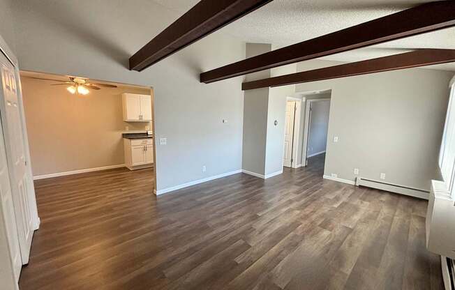 A room with wooden floors and a kitchen area in the background.
