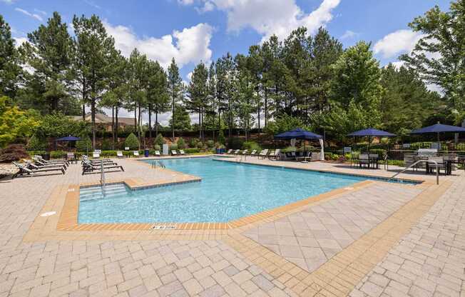 a resort style pool with chairs and umbrellas and trees in the background