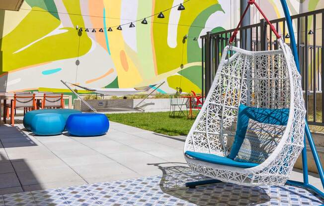 A white hanging chair with blue cushions is in the foreground of a colorful mural.