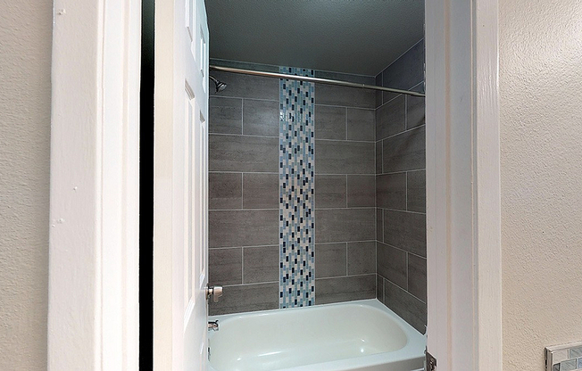 Elegant bathroom featuring a modern bathtub with stylish tile backdrop and mosaic accent for a luxurious touch.