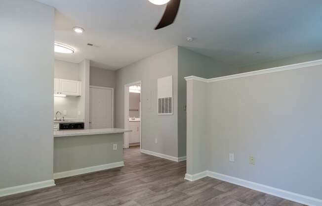 an empty living room with a kitchen and a ceiling fan