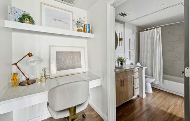 A white chair is in front of a desk with a lamp and picture frame on it.