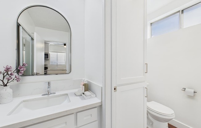 A white bathroom with a sink, mirror, and toilet.