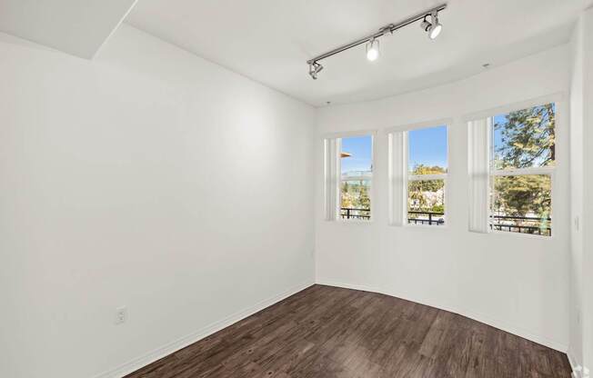 A room with white walls and wooden flooring with three windows.
