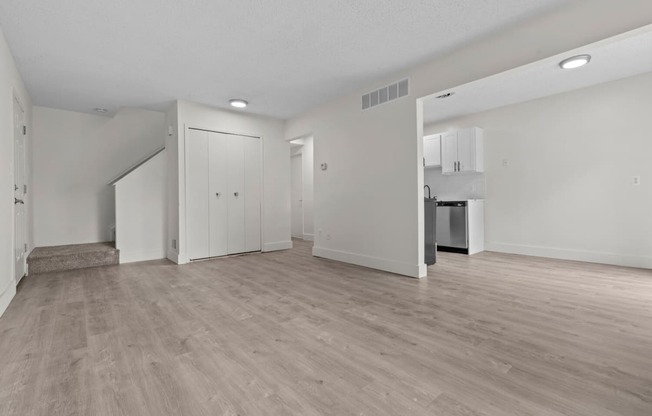 the living room and kitchen of an apartment with white walls and wood flooring