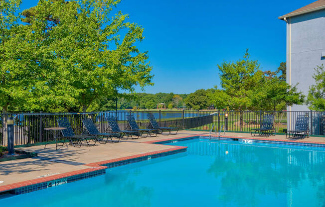 a swimming pool with chaise lounge chairs and trees in the background