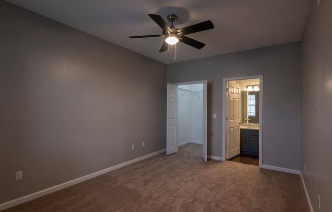 a bedroom with a ceiling fan and a doorway to a bathroom
