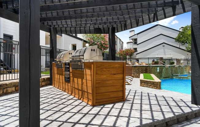 an outdoor barbecue area with a pool in the background and a pergola in the foreground
