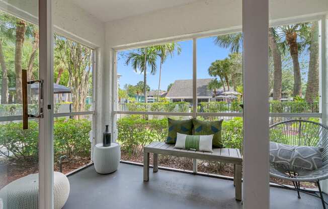 a screened porch with a bench and chairs and a view of palm trees