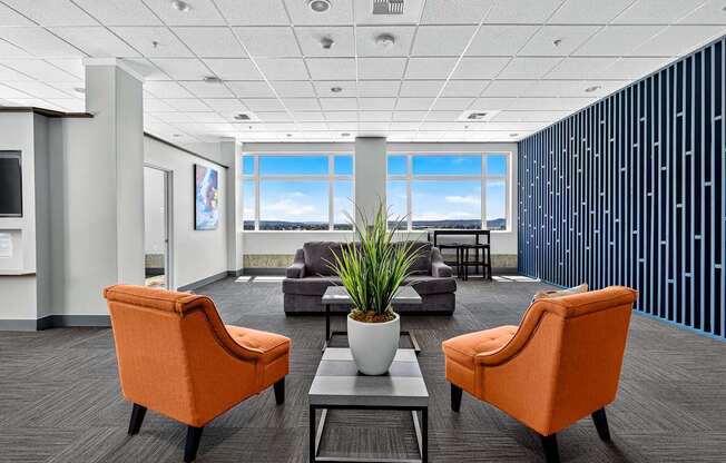 A modern office with orange chairs and a view of the sky through the window.