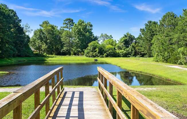 A wooden bridge leads to a serene lake surrounded by lush greenery.