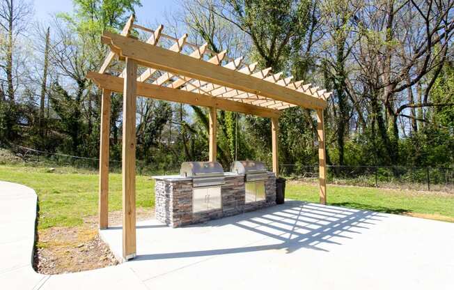 A wooden pergola structure is situated over a stone bench in a park.