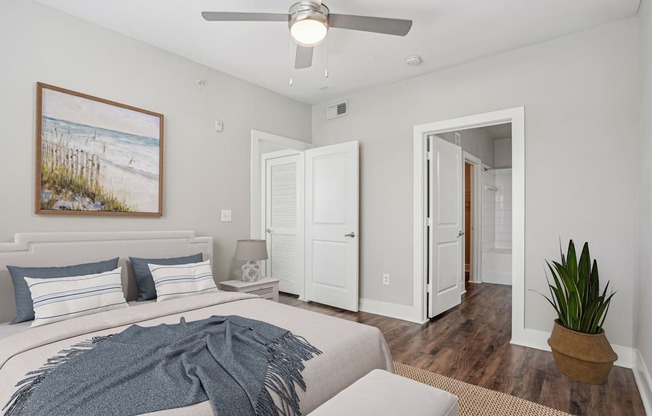A bedroom with a bed, a ceiling fan, and a painting on the wall.