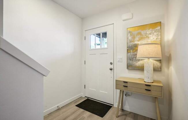 a entryway with a white door and a desk with a lamp