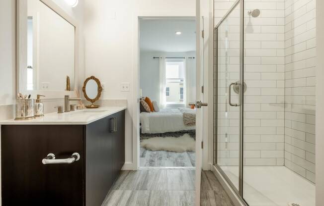 Model bathroom with a shower and a sink and a bedroom