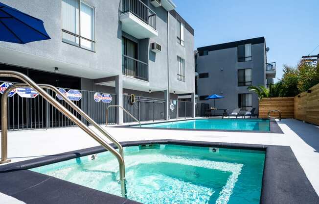 a swimming pool with a blue umbrella in front of an apartment building