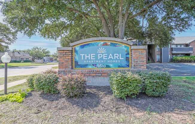 A sign for The Pearl Apartment Homes stands in front of a tree.
