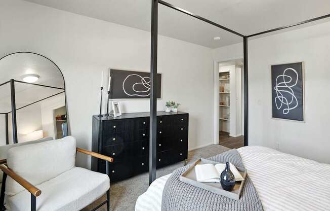 A modern bedroom with a four poster bed, a chair and a dresser.