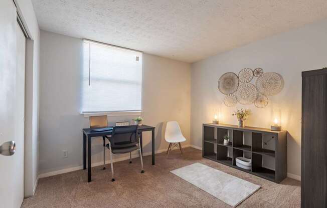 A room with a desk, chair, and shelves with decorative items.