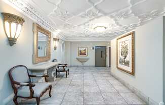 A hallway with a chair, a table, and a painting on the wall.