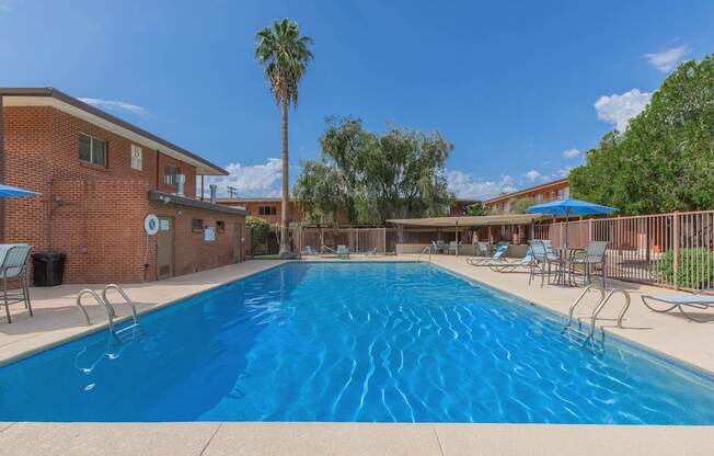 A large blue swimming pool surrounded by a fence and chairs.