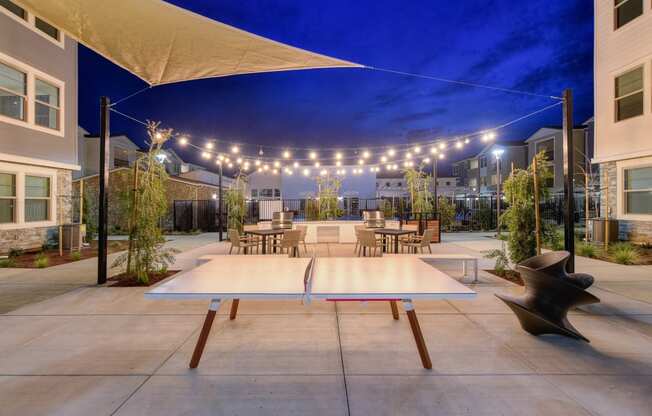 Ping pong table at night with a view of the white lights strung back and forth across the BBQ area at Morgan Ranch Apartments, California