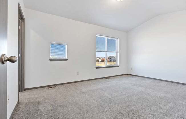 A room with a carpeted floor and two windows.