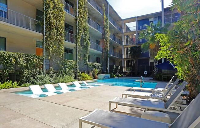 the pool area of an apartment building with a pool and lounge chairs