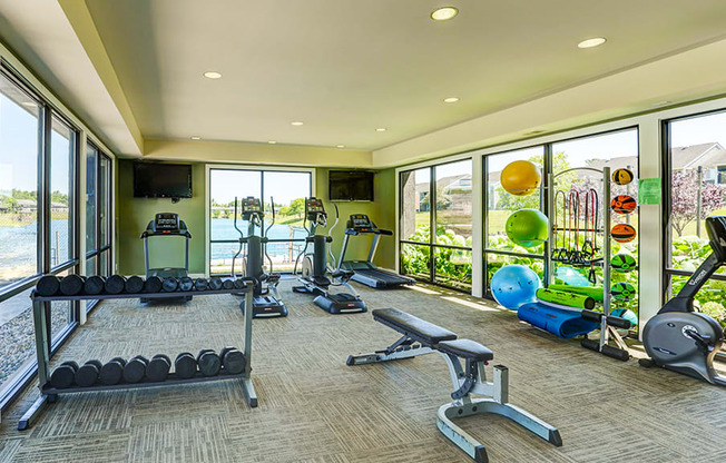 Fitness center at Somerset Lakes Apartments, featuring dumbbells, a bench press, and cardio workout equipment.