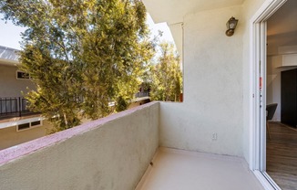 a balcony with a white wall and a tree in the background